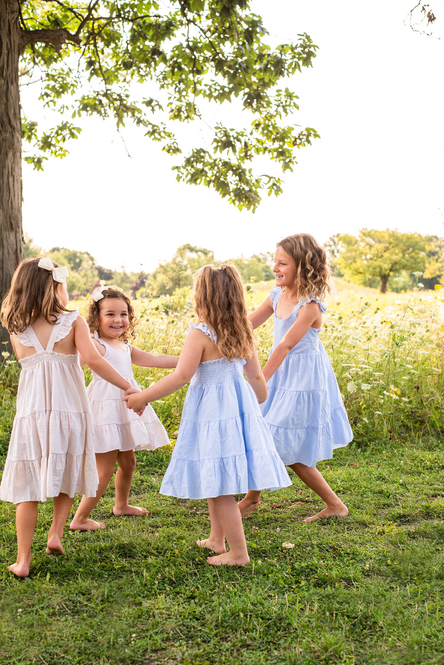 Little girls in white and blue dresses playing together on grassy hill during golden hour.