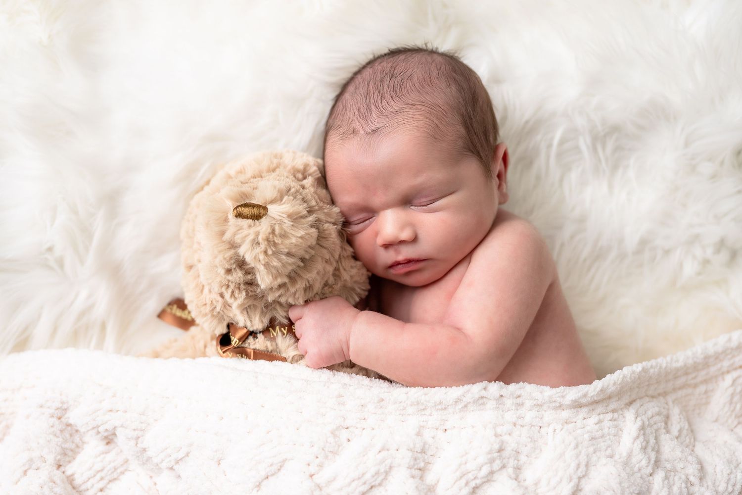 Sleeping newborn baby wrapped in white blanket on soft furry backdrop.