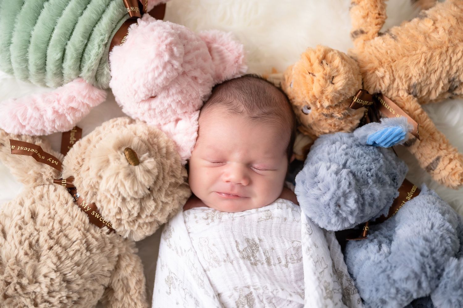 Sleeping baby surrounded by soft plush teddy bears in pastel colors.