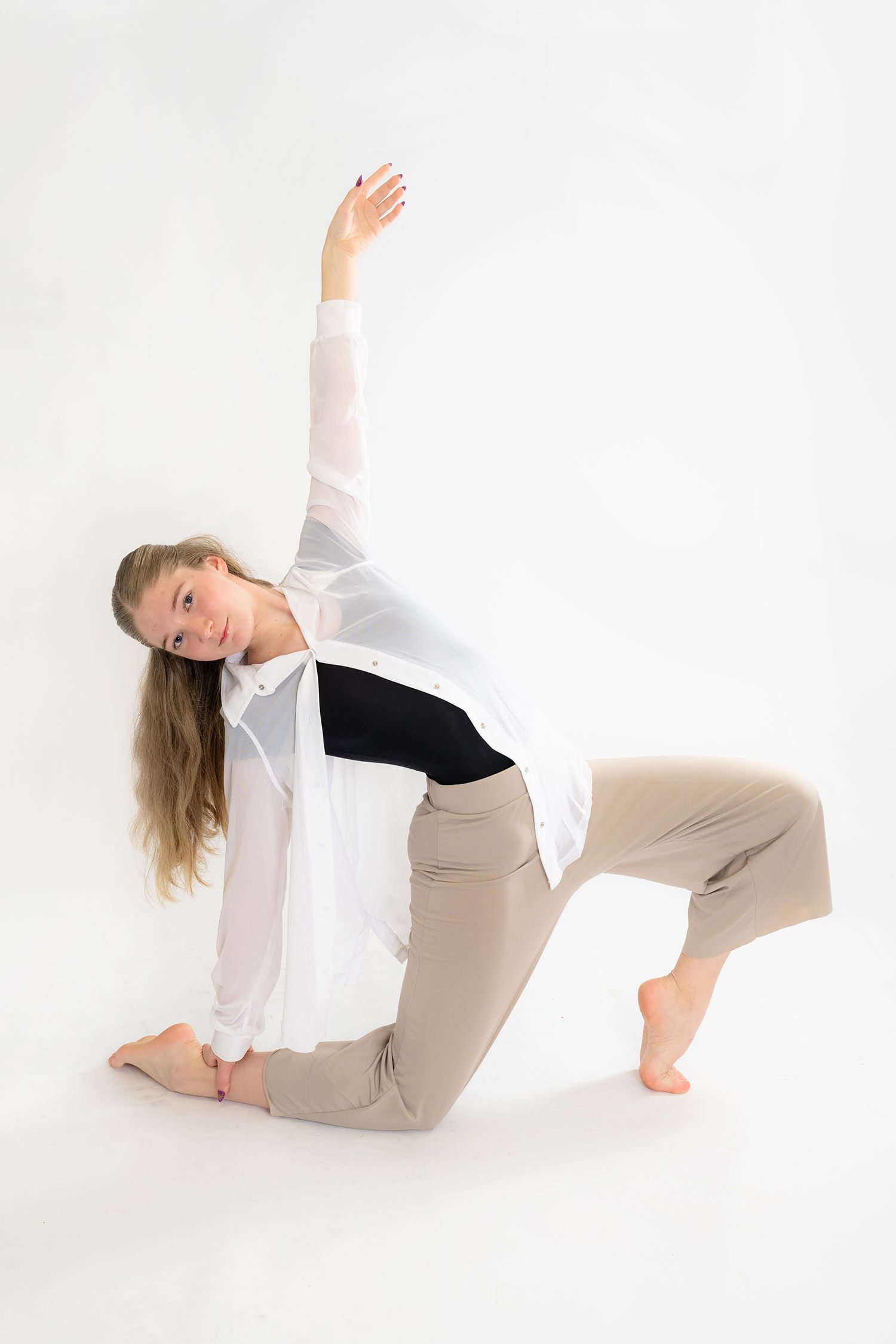Young woman in white shirt and beige pants performing a graceful dance pose against a white background.