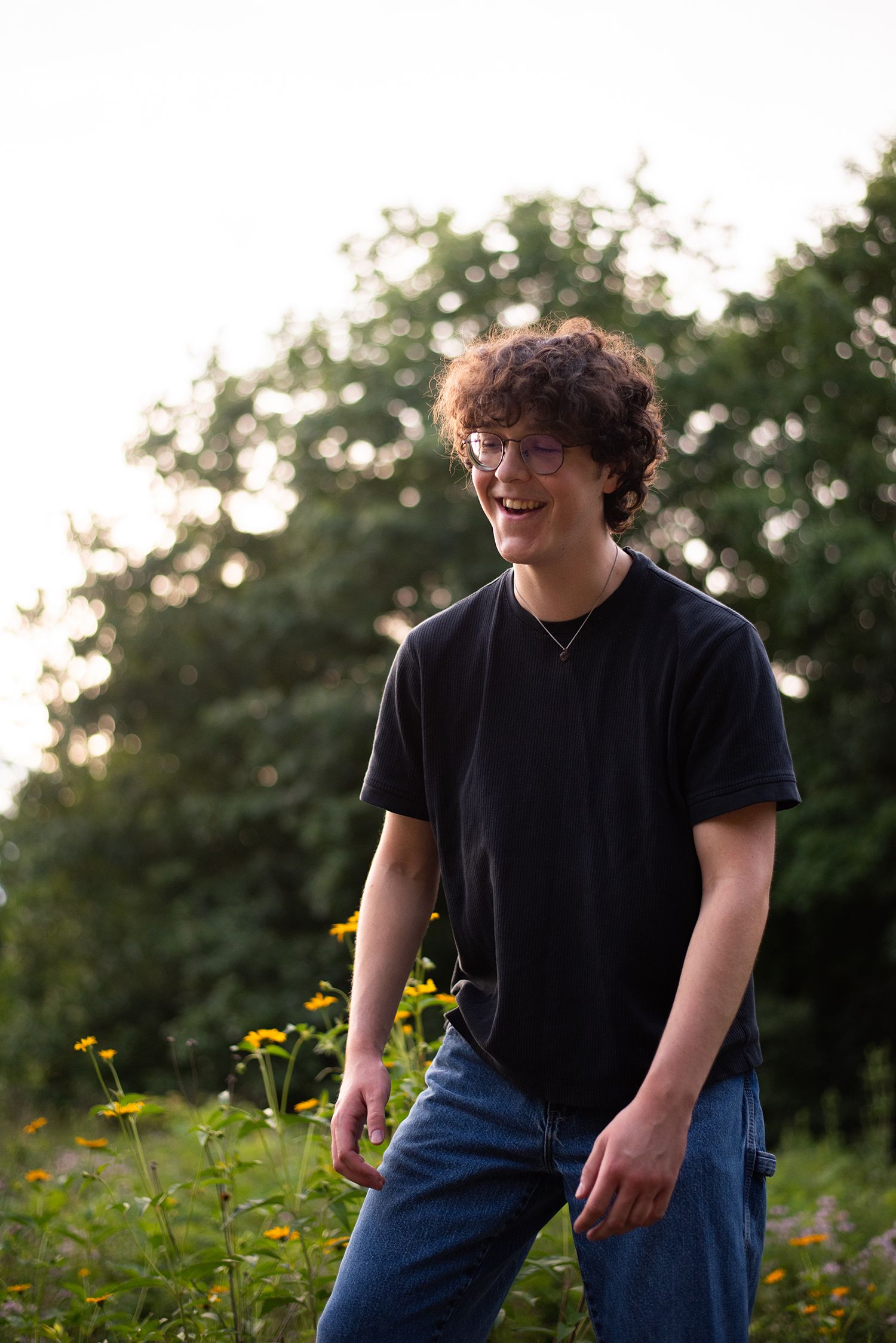 Person in black shirt poses casually in field of yellow wildflowers during golden hour.
