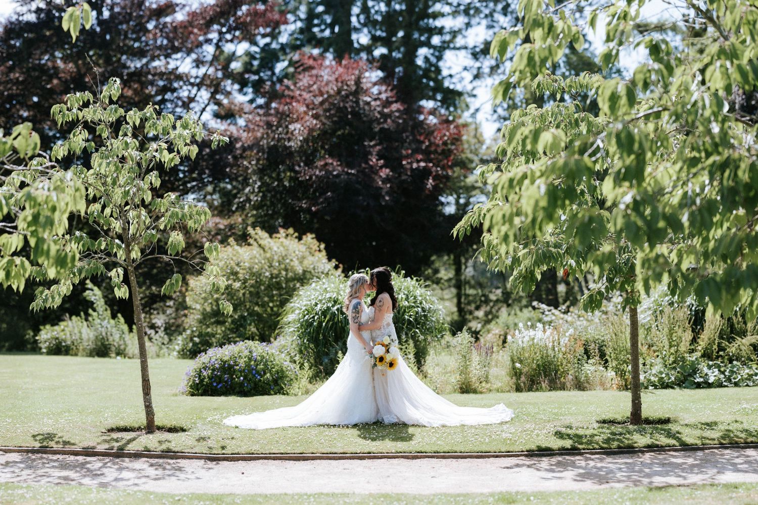 Fasque Castle Wedding Photography. A couple in white dresses poses together in a lush outdoor garden setting.