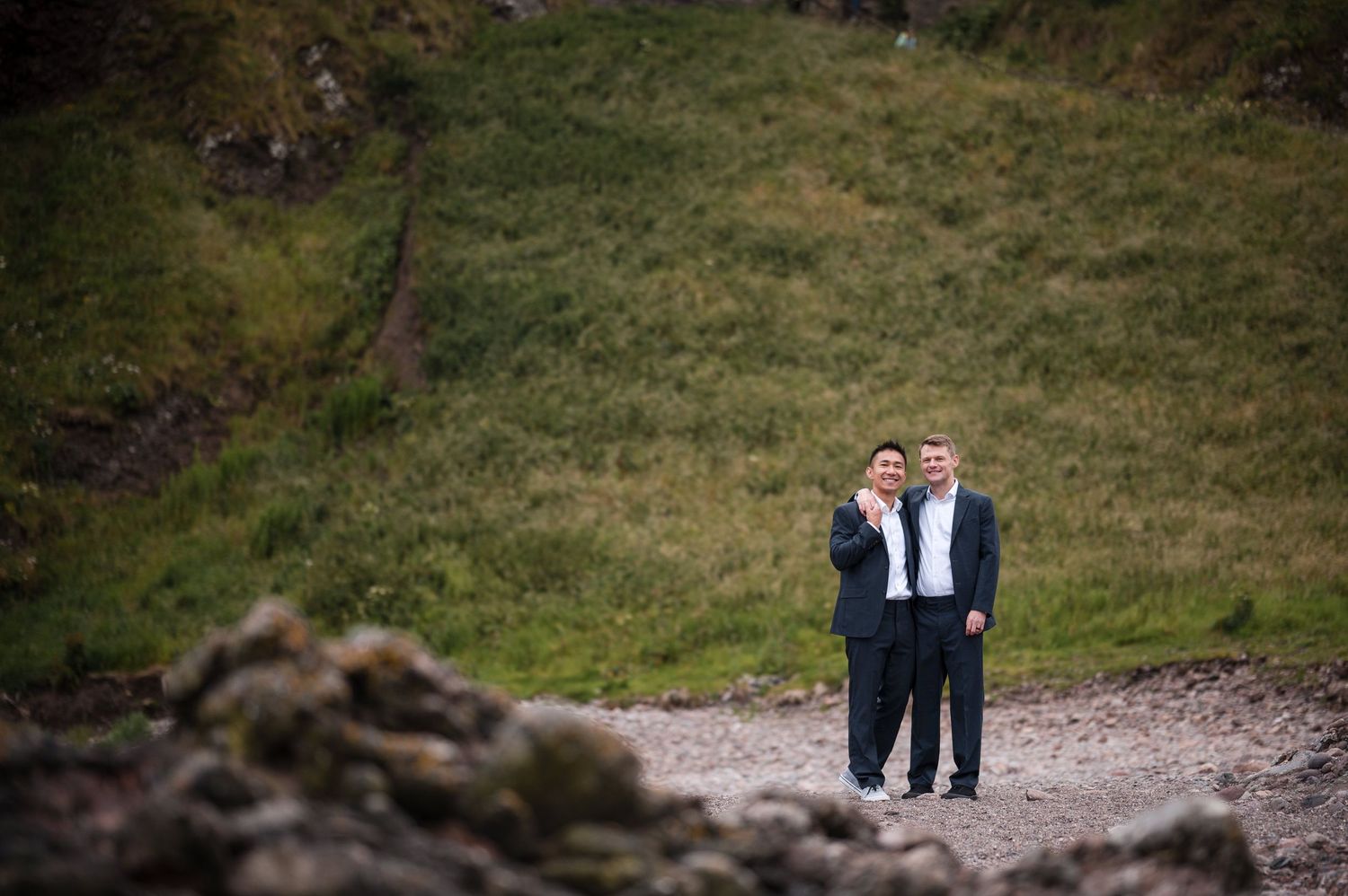 Same Sex Wedding Photography. Two people share an intimate moment on a rugged coastal path overlooking dramatic cliffs and ocean views.