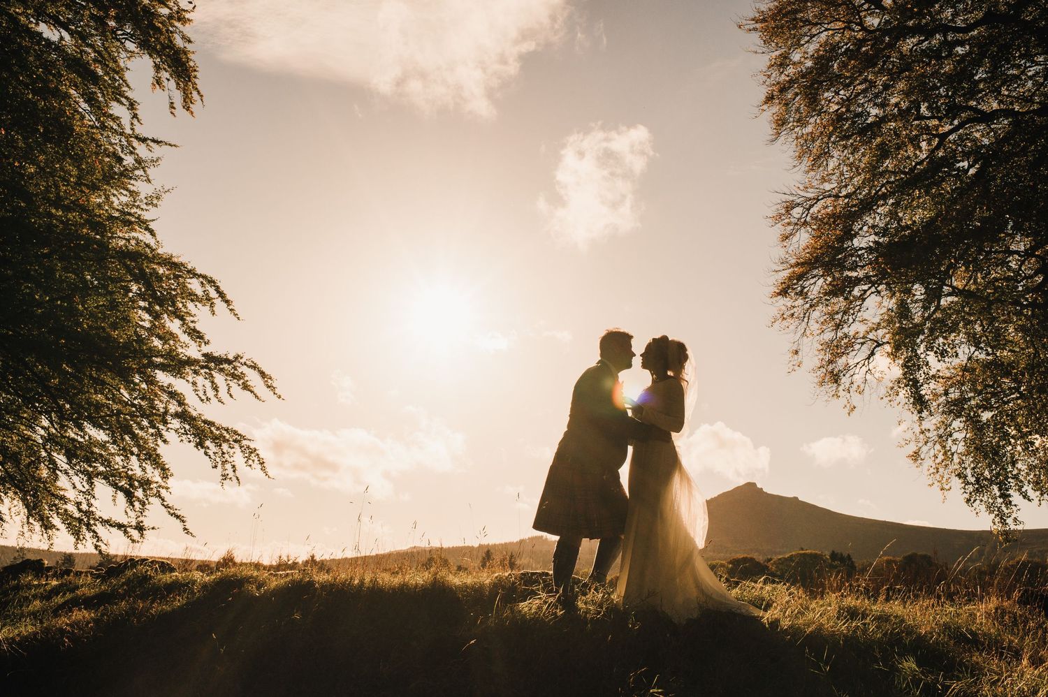 Aberdeen Wedding Photography. Silhouettes of a couple against a warm sunset sky with mountain landscape in the distance.