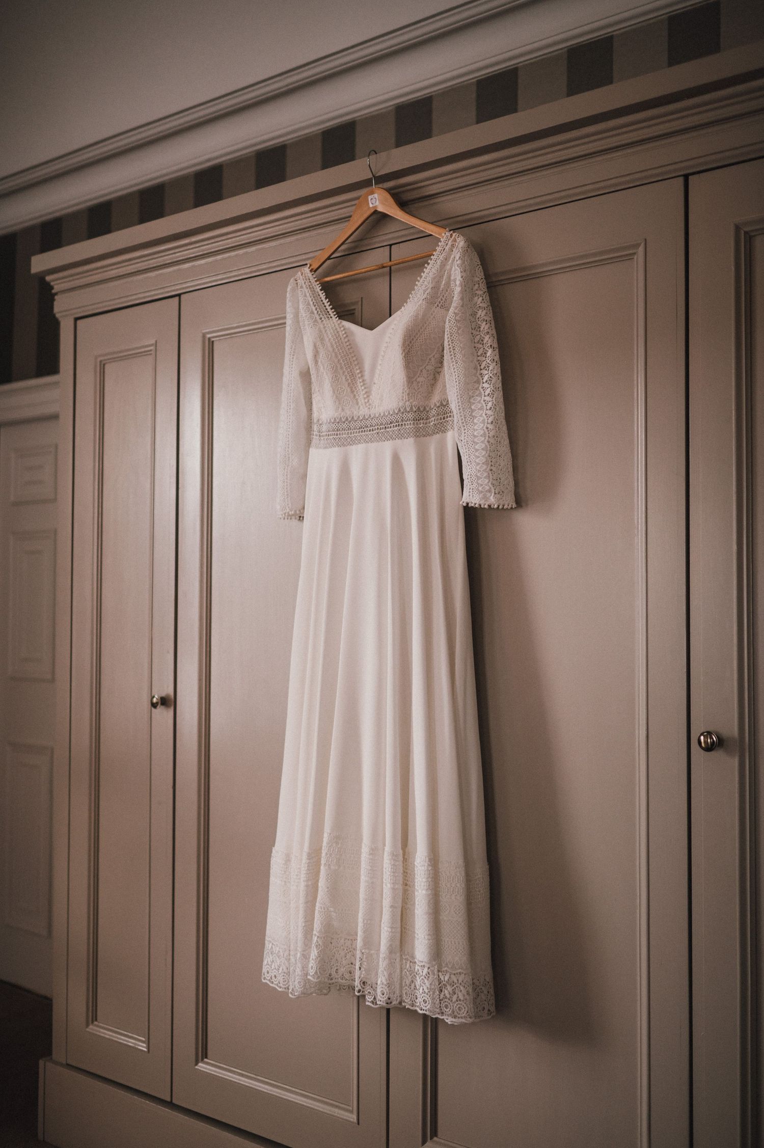 Romantic white wedding gown with lace details hanging on wooden hanger.