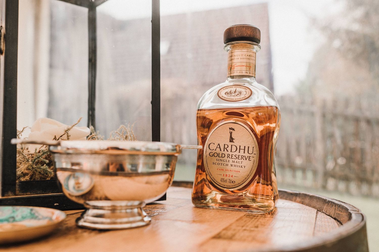 A bottle of Cardhu whiskey with a cocktail glass on a tray by a window.