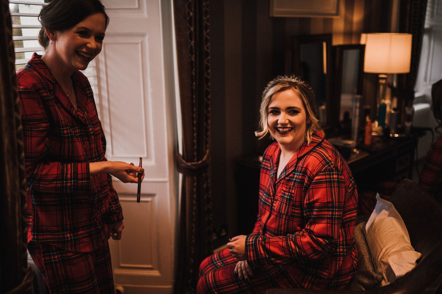 Two people wearing matching red plaid flannel shirts share a candid moment in a cozy indoor setting.