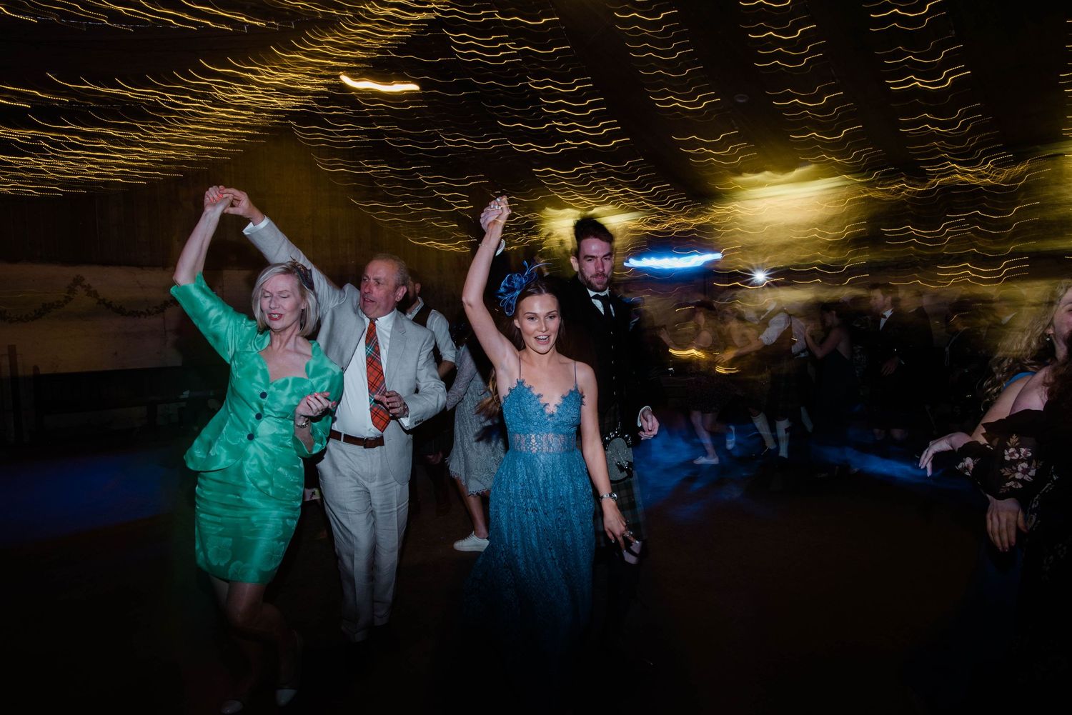 Wedding guests dance energetically under moody lighting at an indoor celebration.