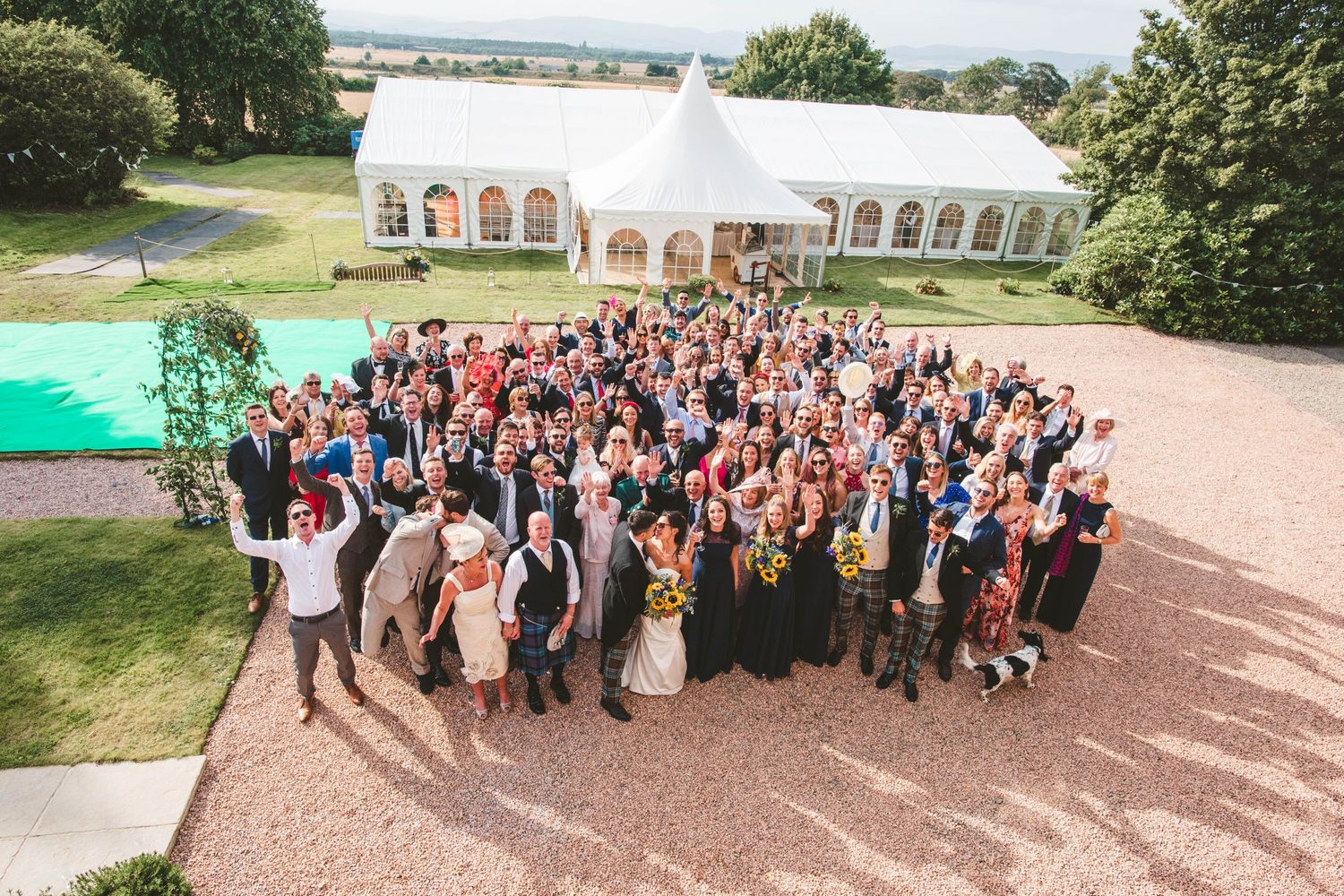 Large group of wedding guests pose together in front of an elegant white tent venue.