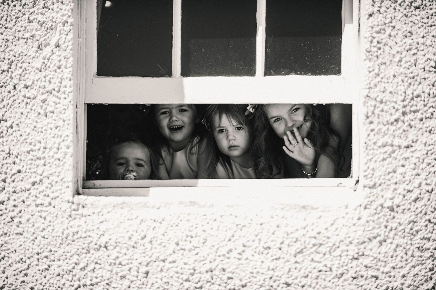 Black and white photo of children peeking and waving through a window.