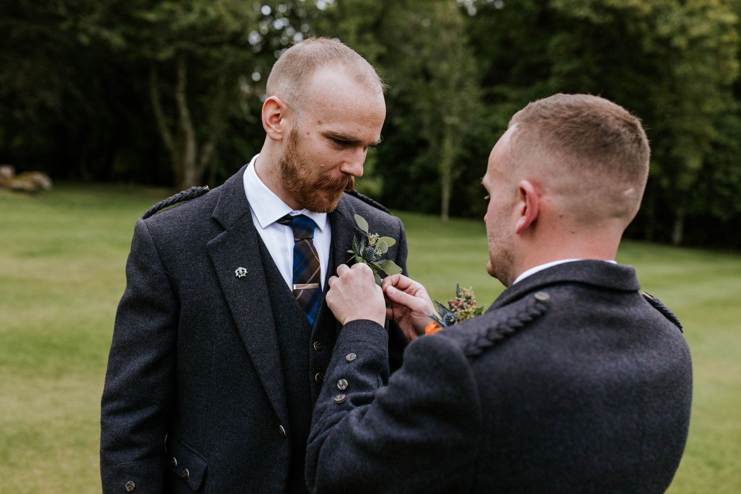 Wedding party members in dark suits share emotional moments outdoors.