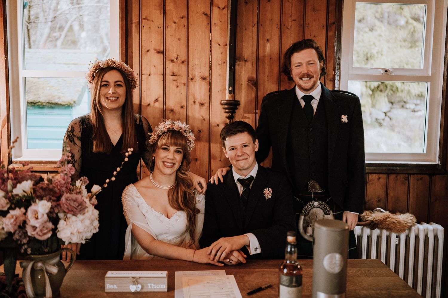Wedding party poses at wooden table decorated with pink flowers and vintage decor.
