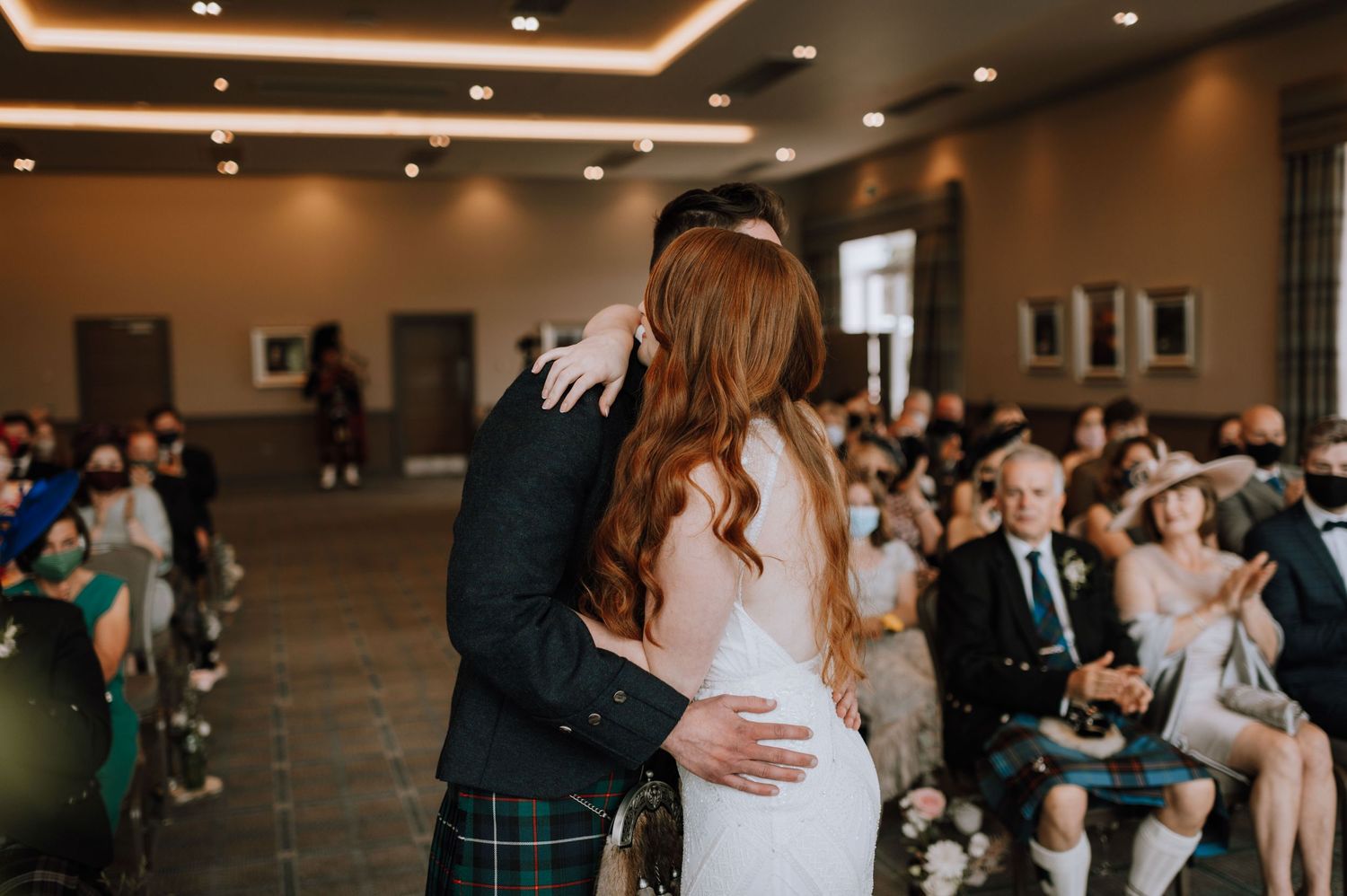 Romantic embrace during wedding ceremony with Scottish kilt and white gown.