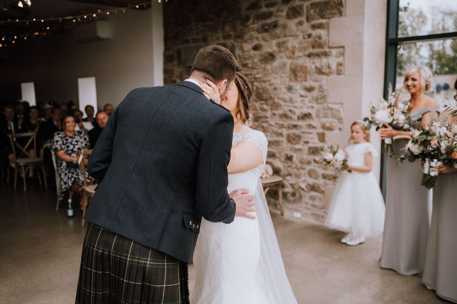 A couple shares their first dance at a rustic stone-walled wedding venue while guests look on.