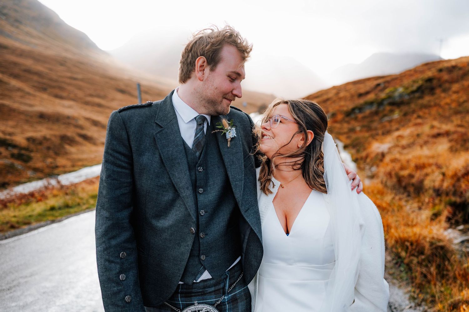 A joyful wedding moment captured on a rainy road in the Scottish Highlands.