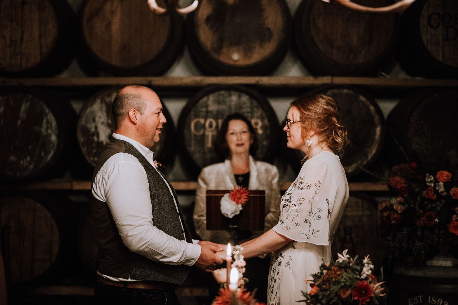 Intimate wedding ceremony in a wine barrel room with romantic lighting.