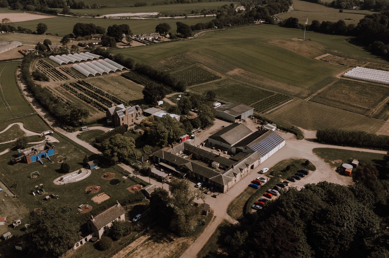 Aerial view of a rustic estate with multiple buildings and sports fields surrounded by countryside.
