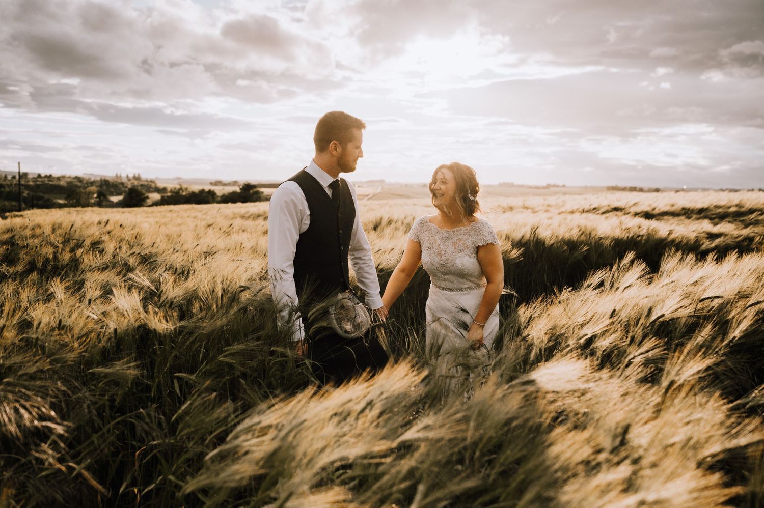 Newlyweds stand together in a sun-kissed field of tall grass during golden hour.
