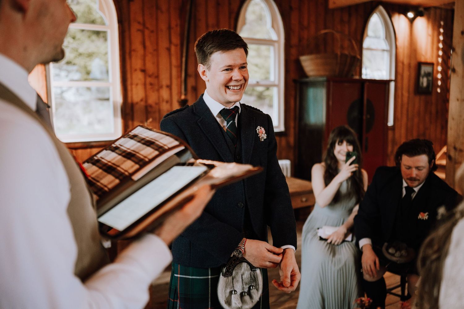 A joyful wedding ceremony moment with traditional Scottish kilts and formal attire.