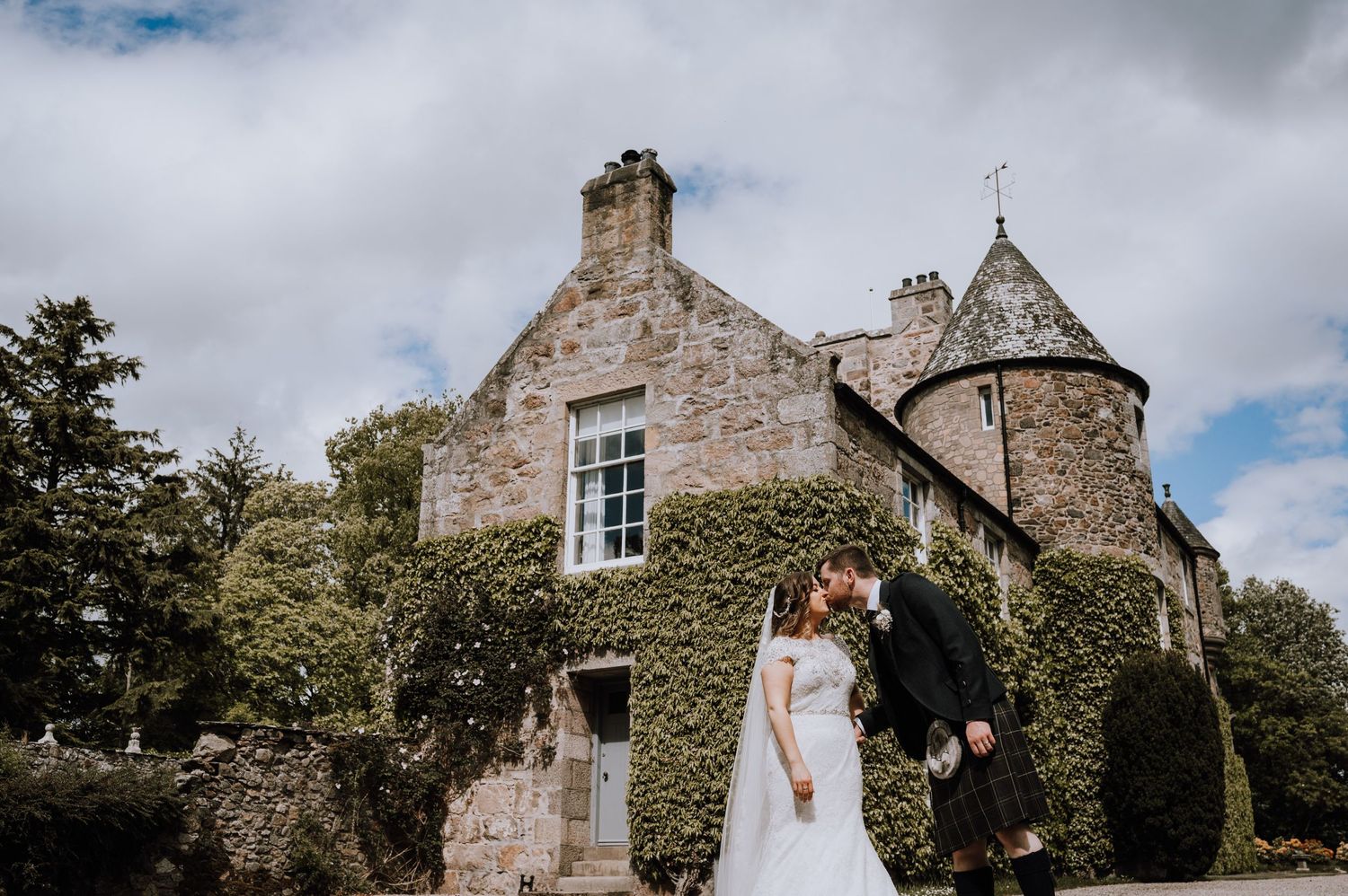 A wedding couple poses in front of a stunning stone castle with ivy-covered walls.
