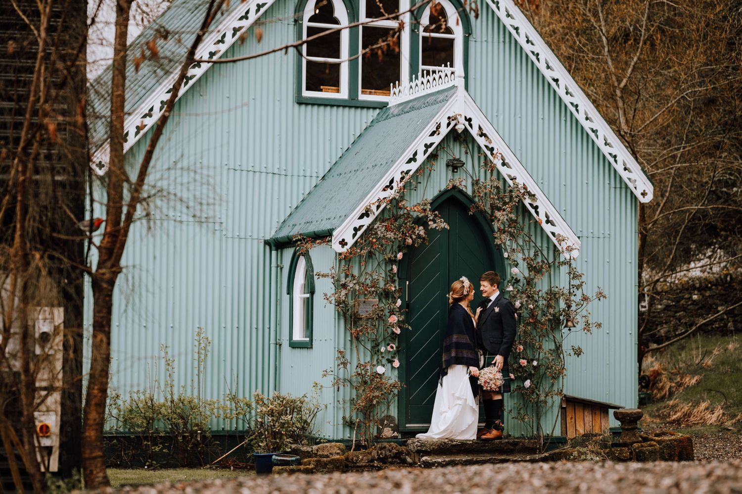 Romantic wedding moment captured at entrance of mint green chapel with Gothic details and climbing vines.