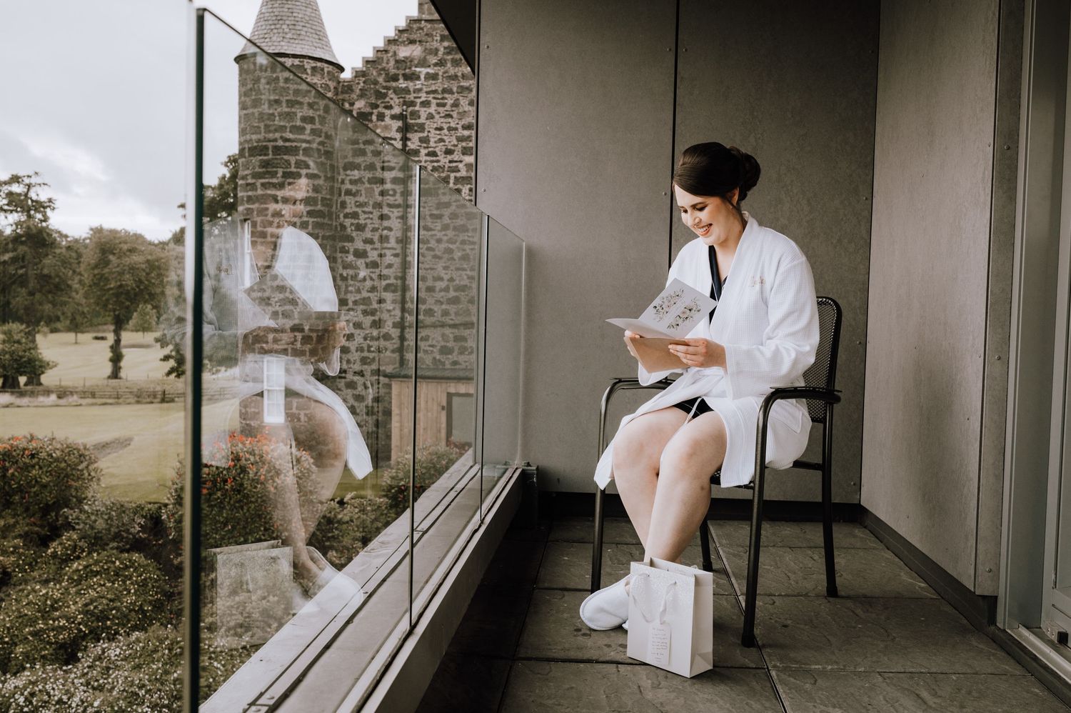 Person in white robe sitting alone on balcony while checking phone.