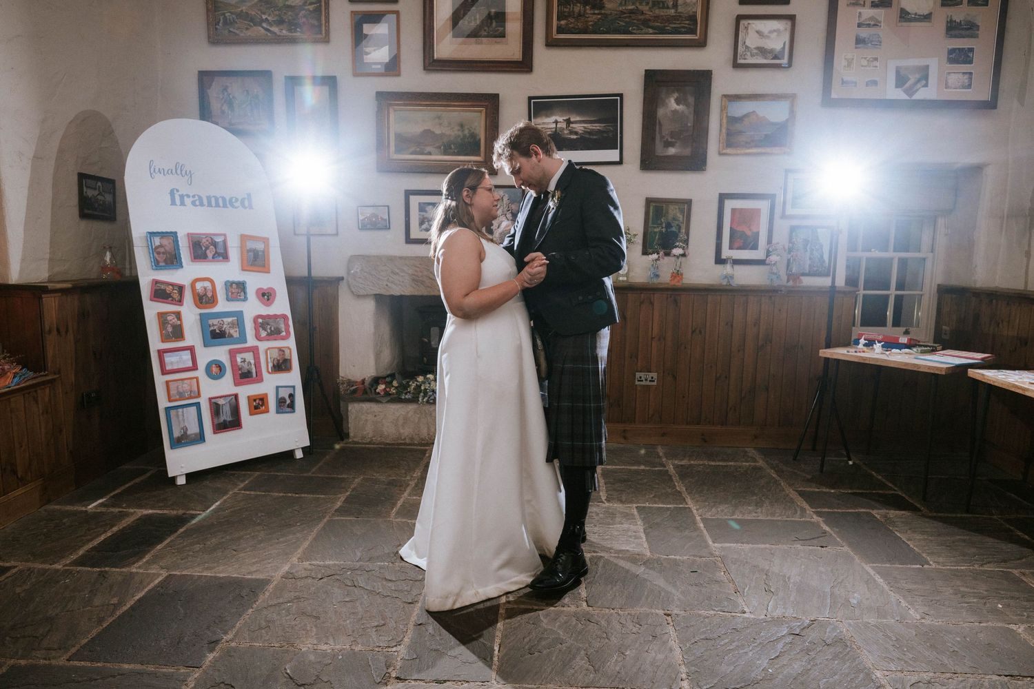 Newlyweds share their first dance in an intimate venue decorated with framed photographs on the walls.