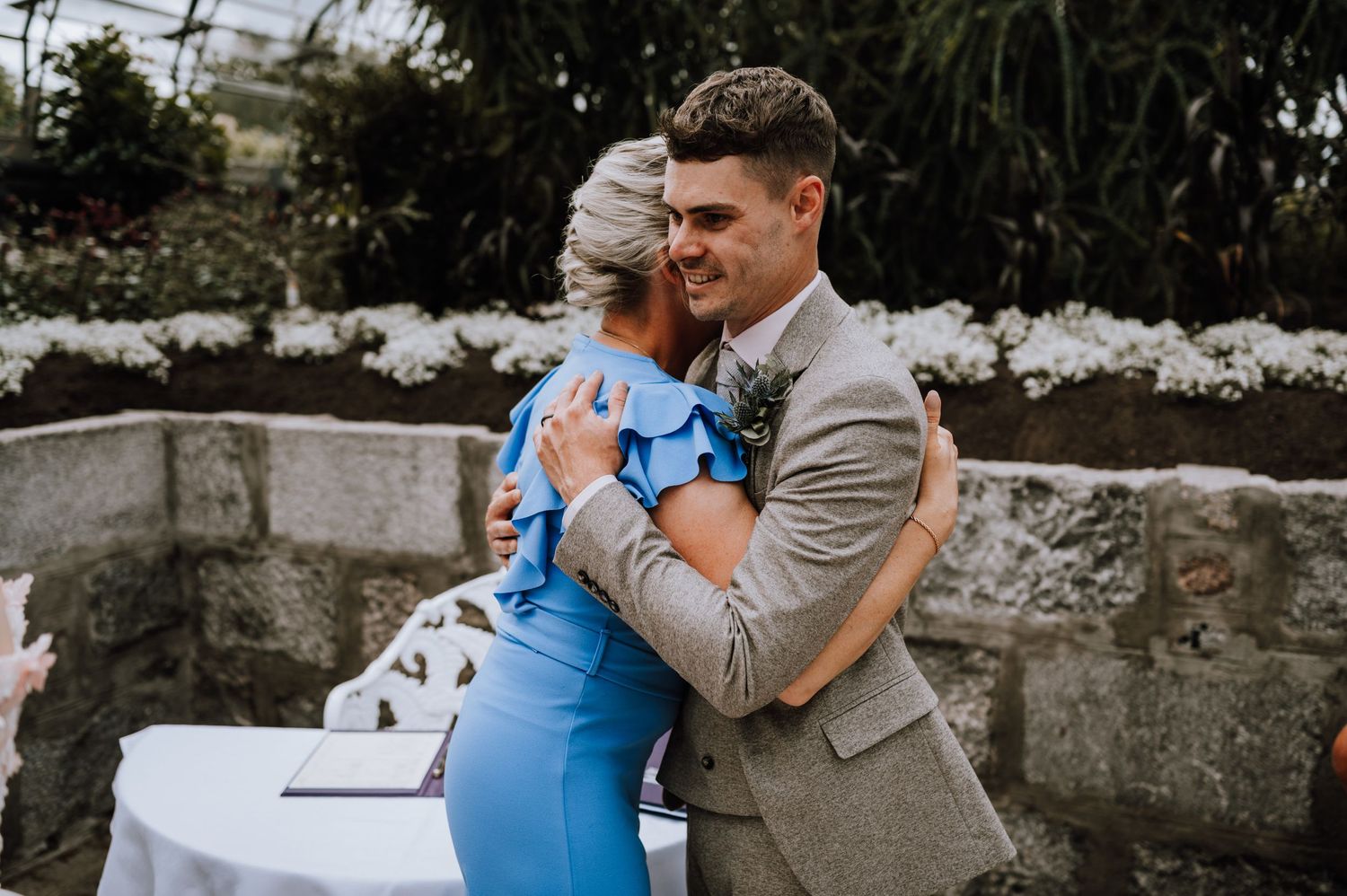 A couple in formal attire share a joyful embrace at an outdoor wedding reception.