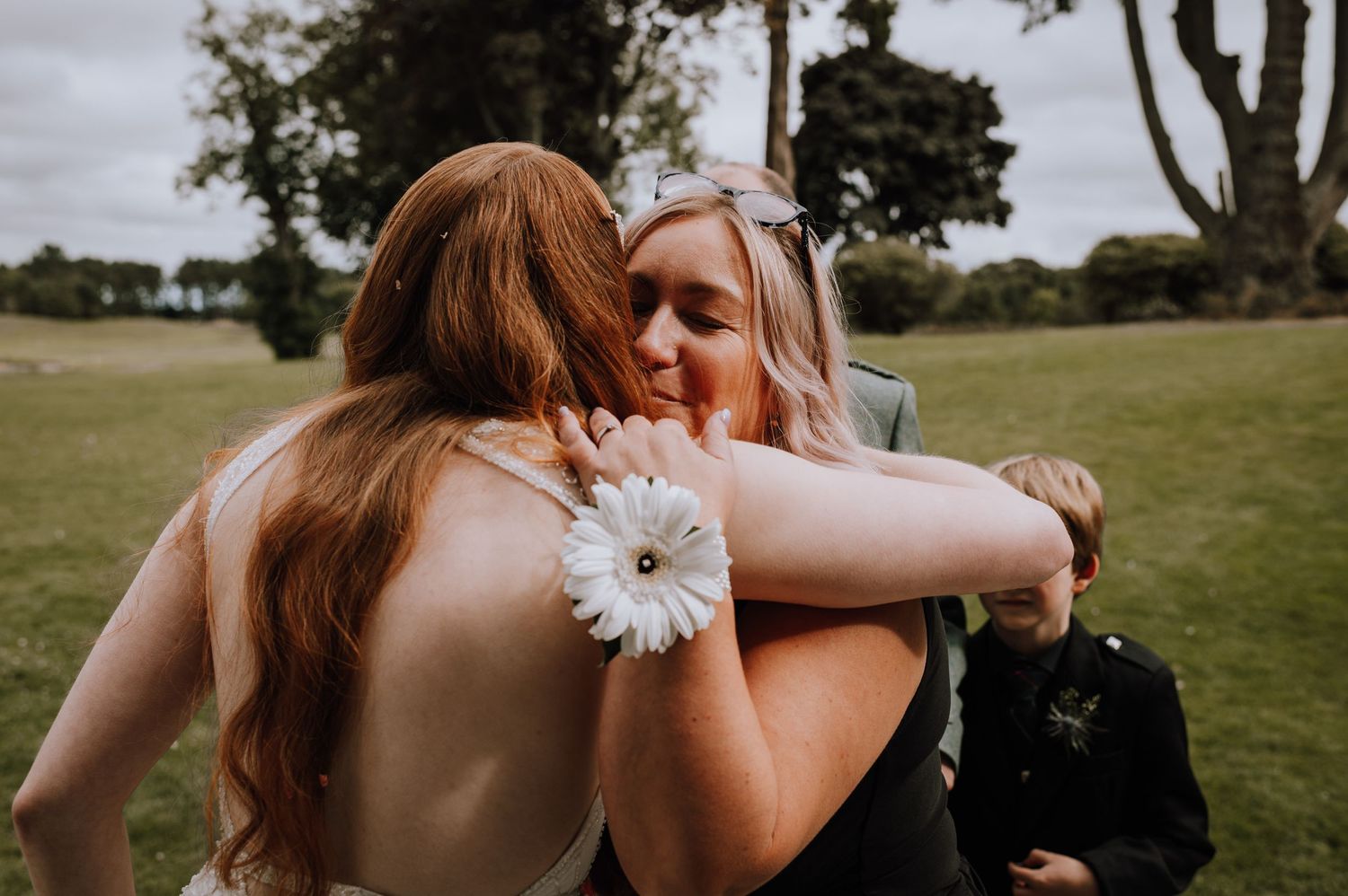 Intimate embrace during outdoor wedding celebration with white flower detail.