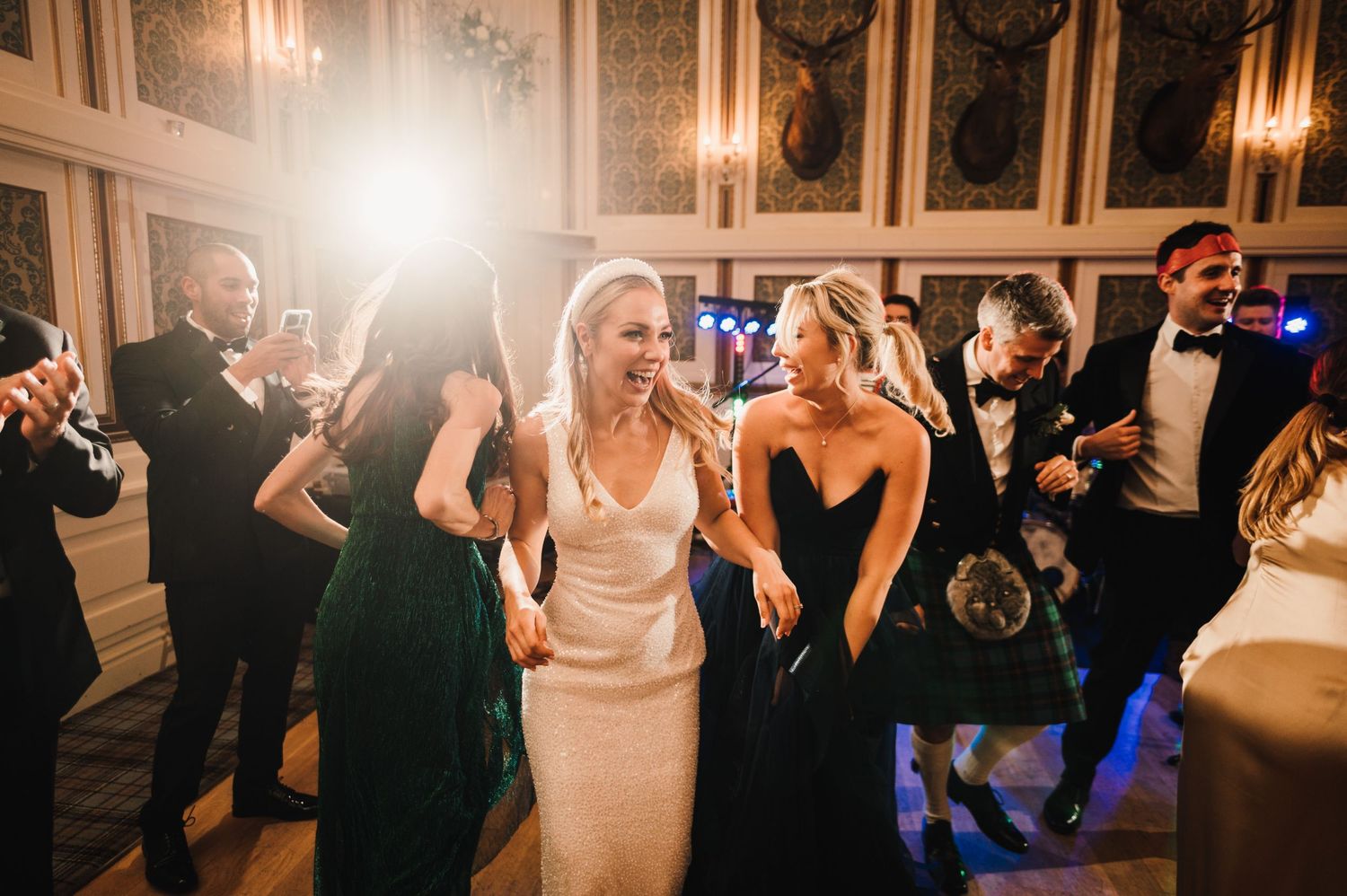 Wedding reception dance party with guests celebrating in an ornate ballroom with chandelier lighting.