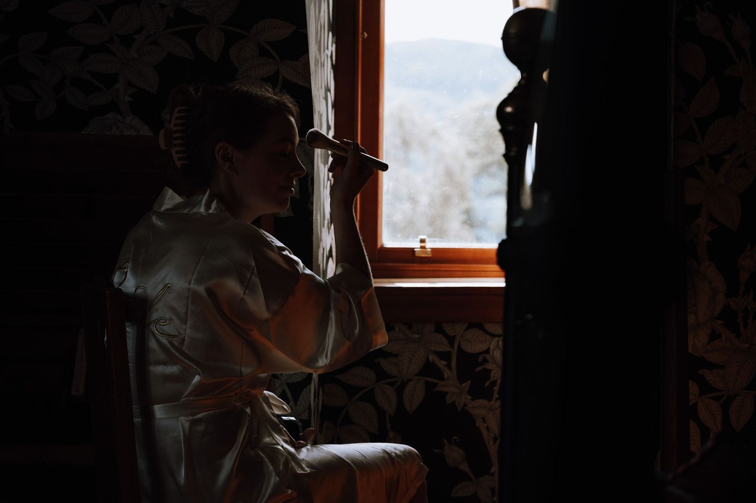 Silhouette by a window with decorative wallpaper in moody morning light.