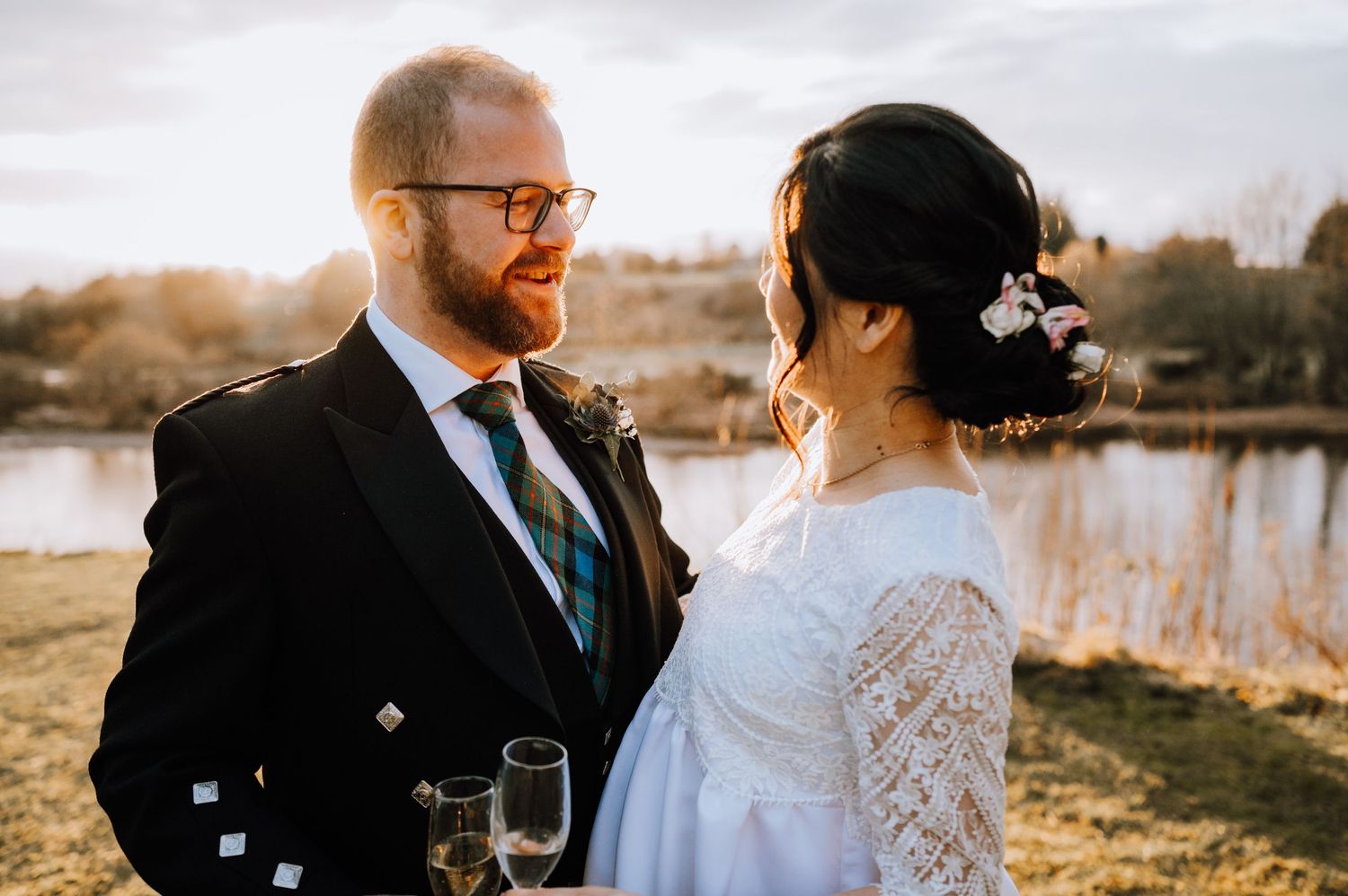 Sunset wedding portrait with couple in Scottish and modern wedding attire by a lake.