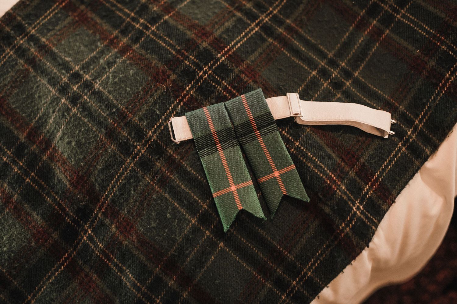 Green and white tartan bow tie placed on plaid fabric.