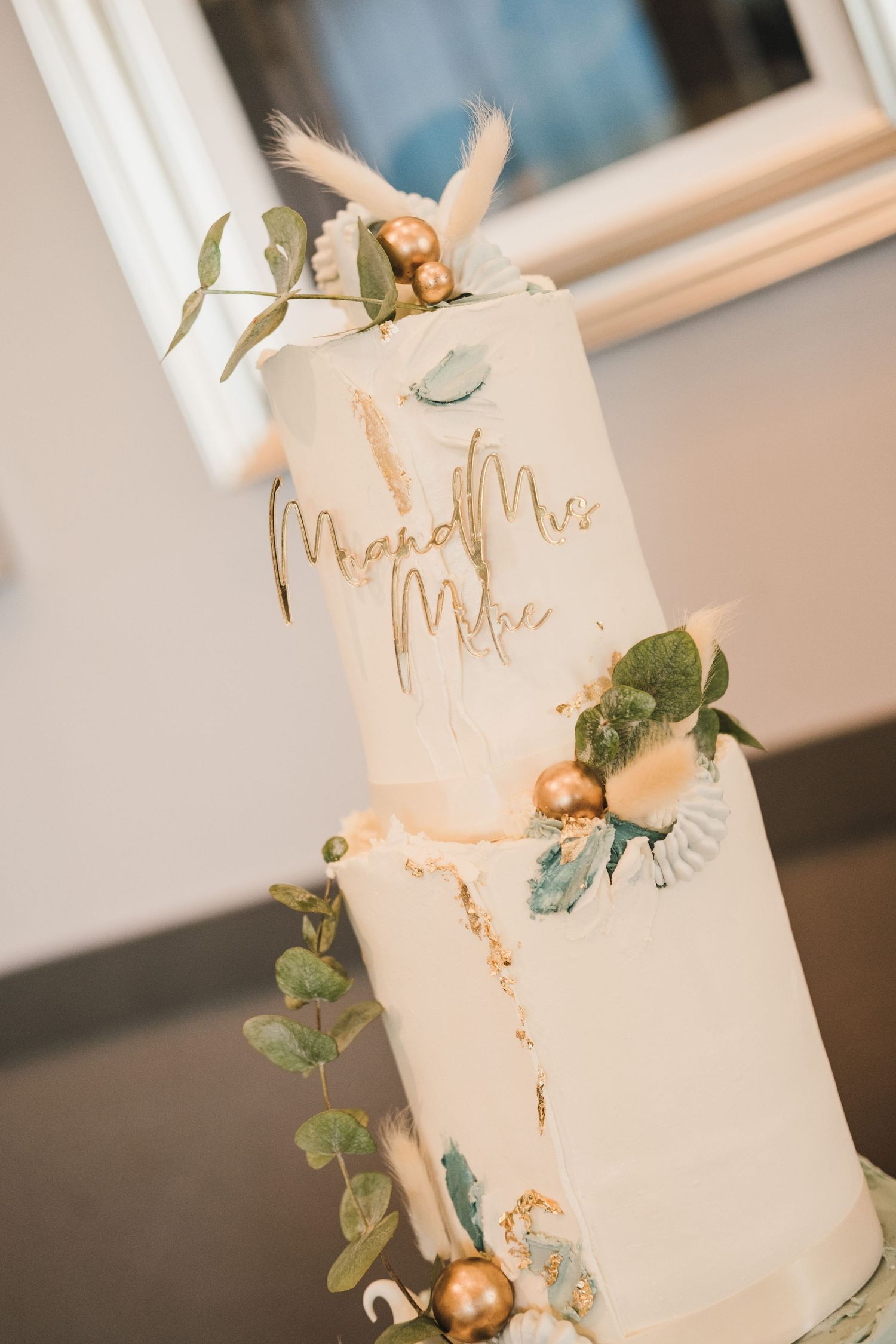 Elegant white wedding cake with gold lettering and floral accents.