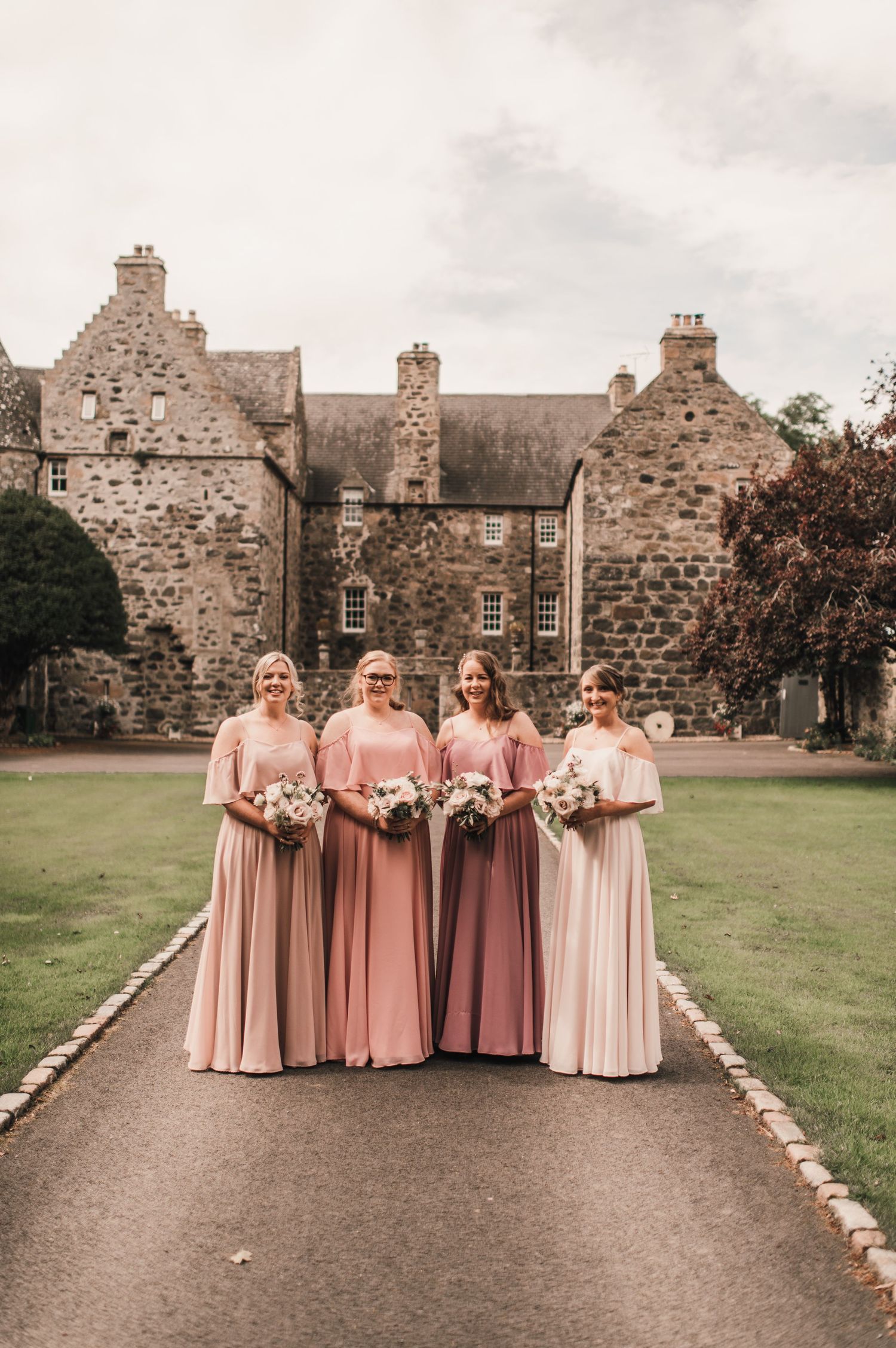 Bridal party in pink dresses standing in front of a historic Scottish stone castle.