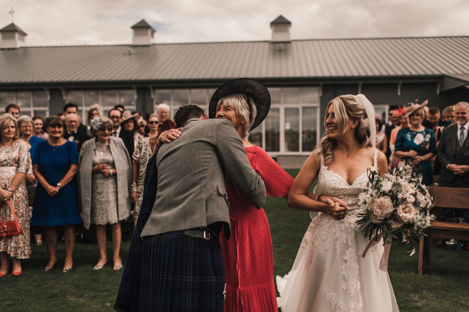 Wedding celebration with guests gathered outdoors at modern venue during emotional ceremony moment.