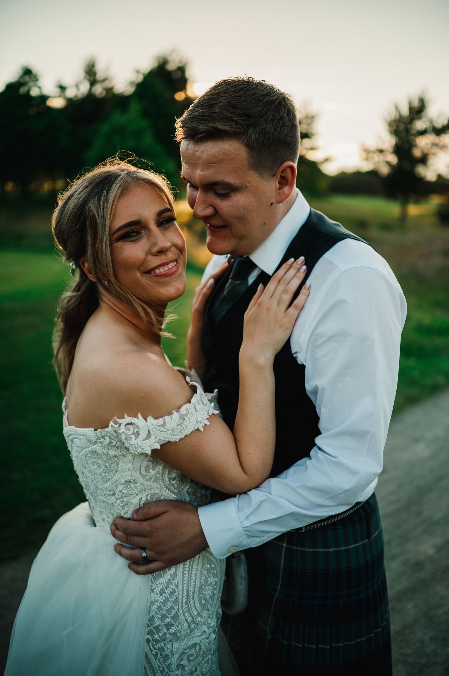 A couple in wedding attire share a close embrace on a golf course during sunset.