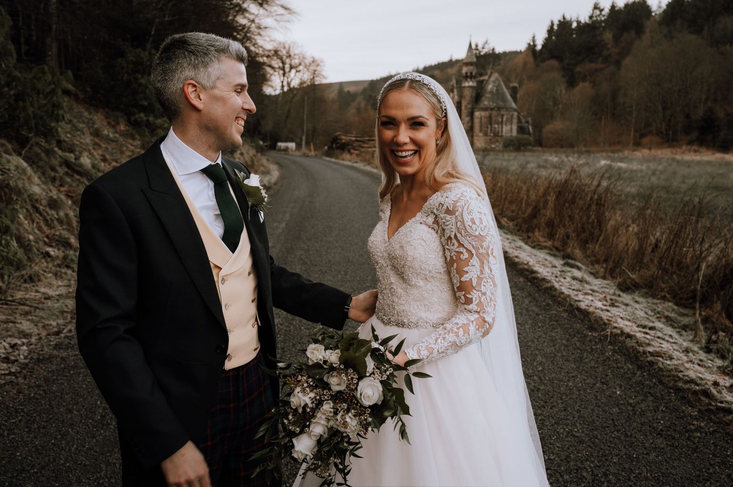 Couple share a romantic moment on a rural path with scenic hills in the background.