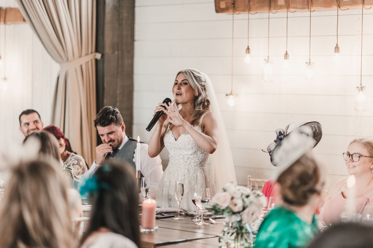 A wedding reception speech moment captured in an elegant indoor venue with hanging lights.