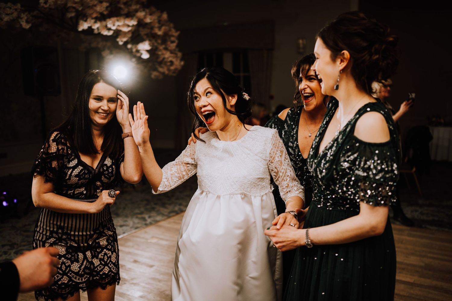 Group of party guests laughing and dancing together on a wooden dance floor at an evening celebration.