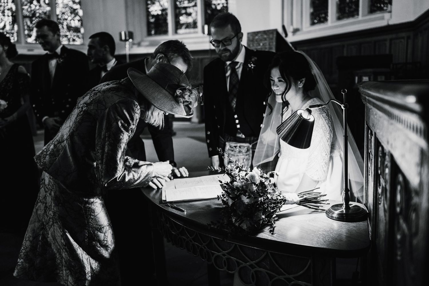Wedding guests sign the registry book in dramatic black and white photography at a church ceremony.