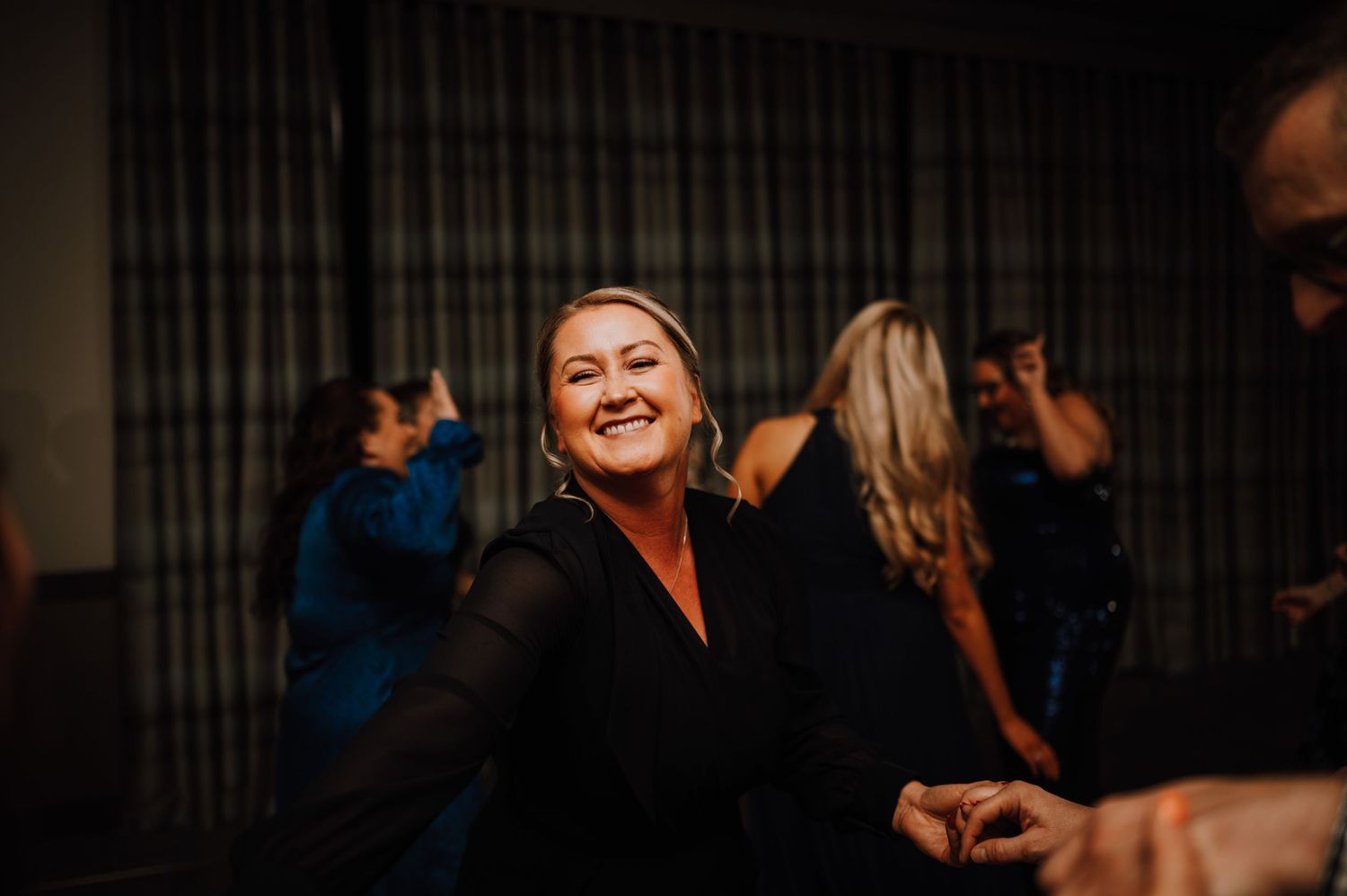 Guest smiles joyfully while dancing at wedding reception in dimly lit venue.