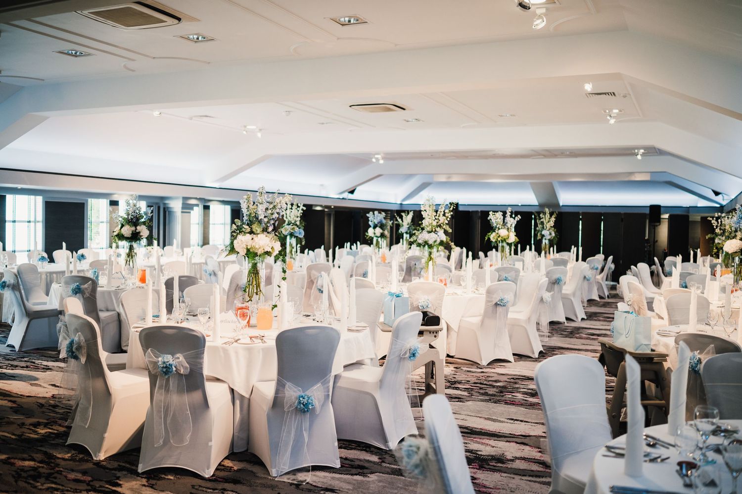 Elegant wedding reception ballroom with white chair covers and formal table settings.