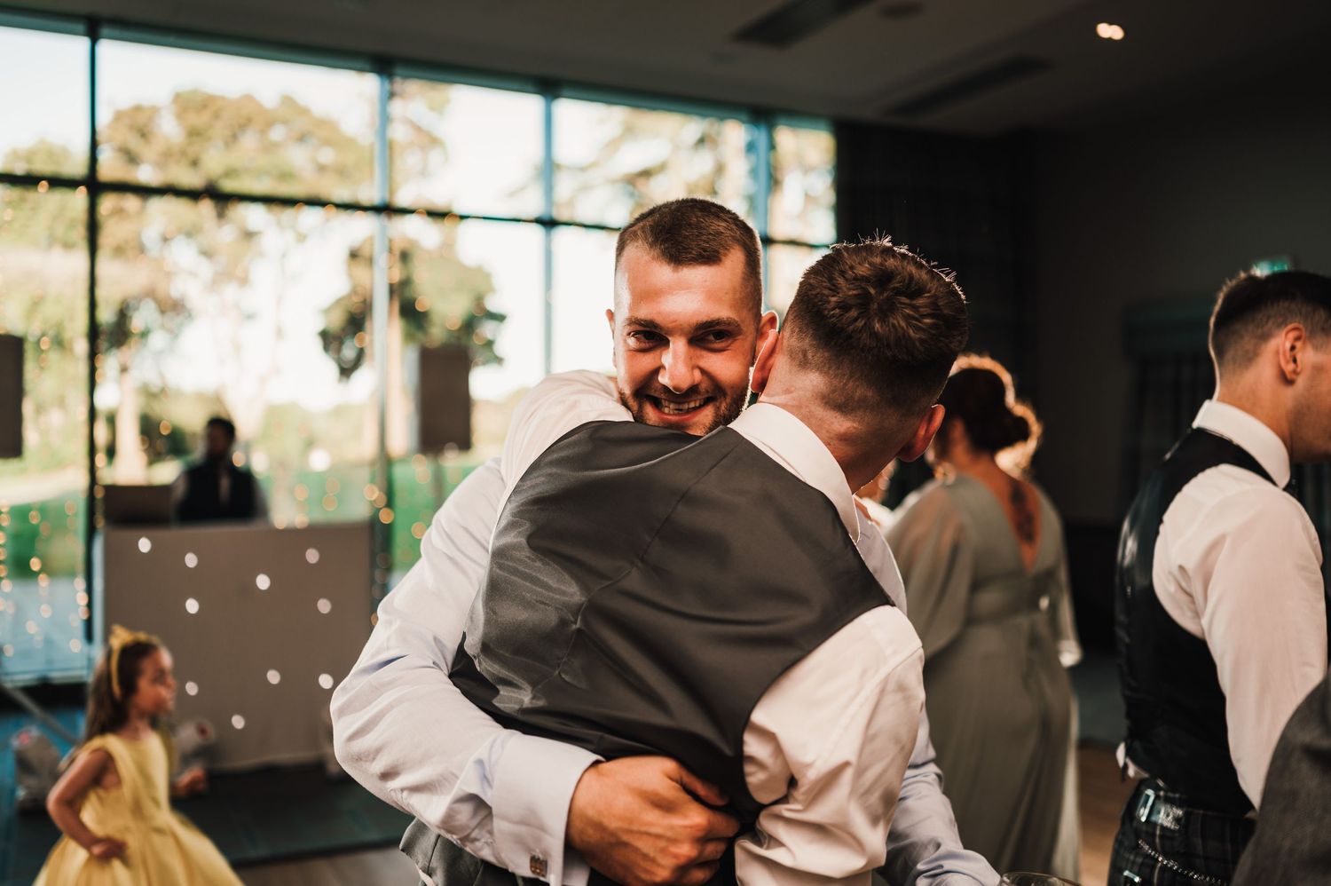 Guests sharing hugs and embraces during a wedding celebration in a modern venue.