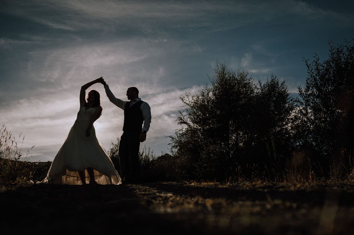 Silhouettes of a couple dancing outdoors against a moody sunset sky.