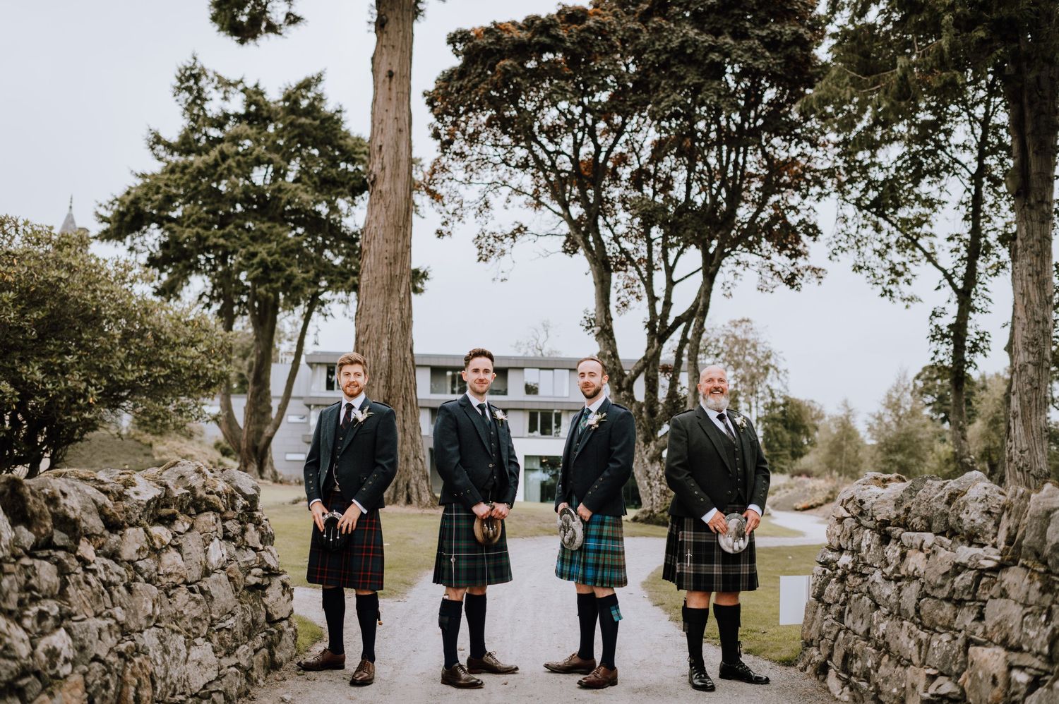 Group wearing traditional Scottish kilts standing on stone path between rock walls.