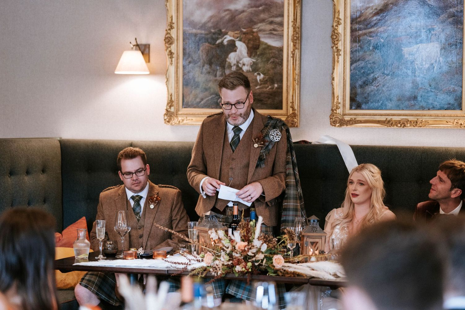 Wedding reception dinner tables set beneath ornate framed artwork in an elegant dining room.