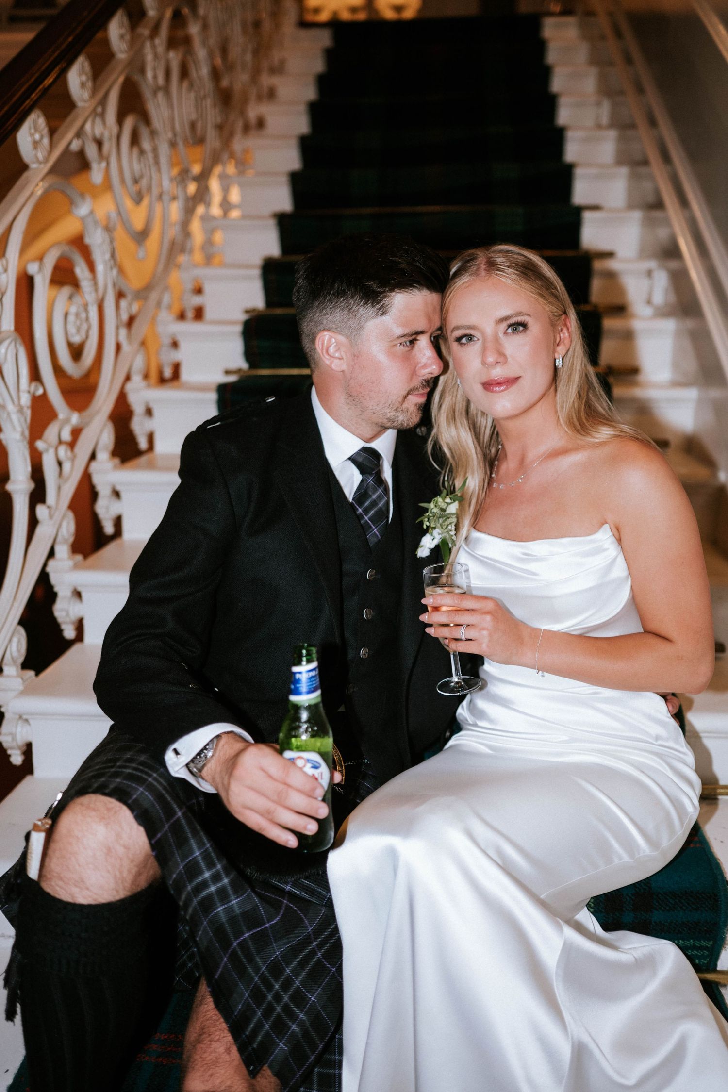 Couple shares intimate moment on ornate staircase during wedding reception.