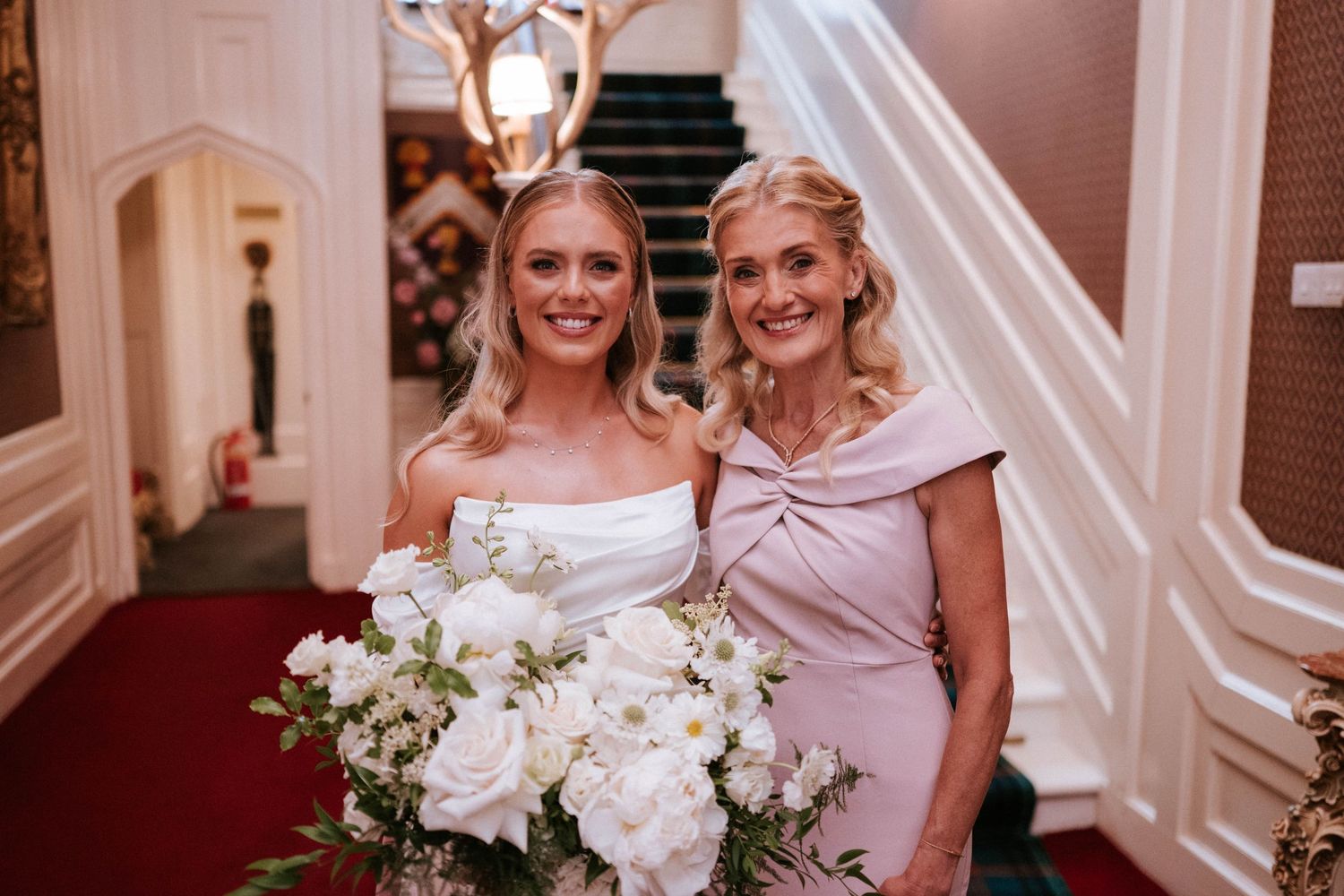Wedding party members sharing smiles and hugs in an elegant white hallway.