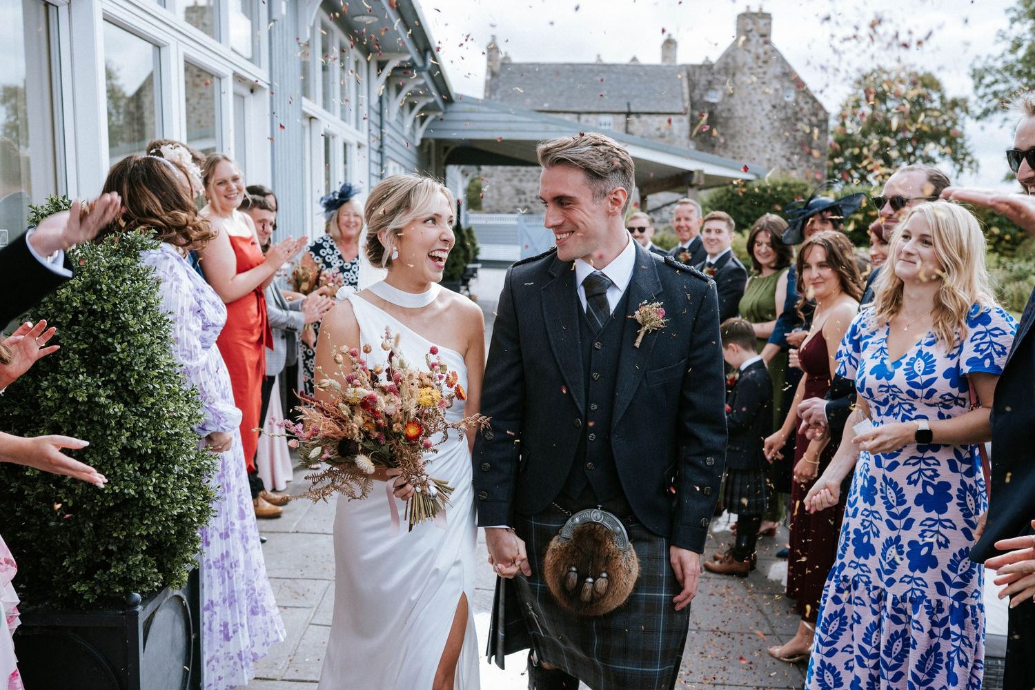 Wedding guests celebrating with confetti outside historic building.